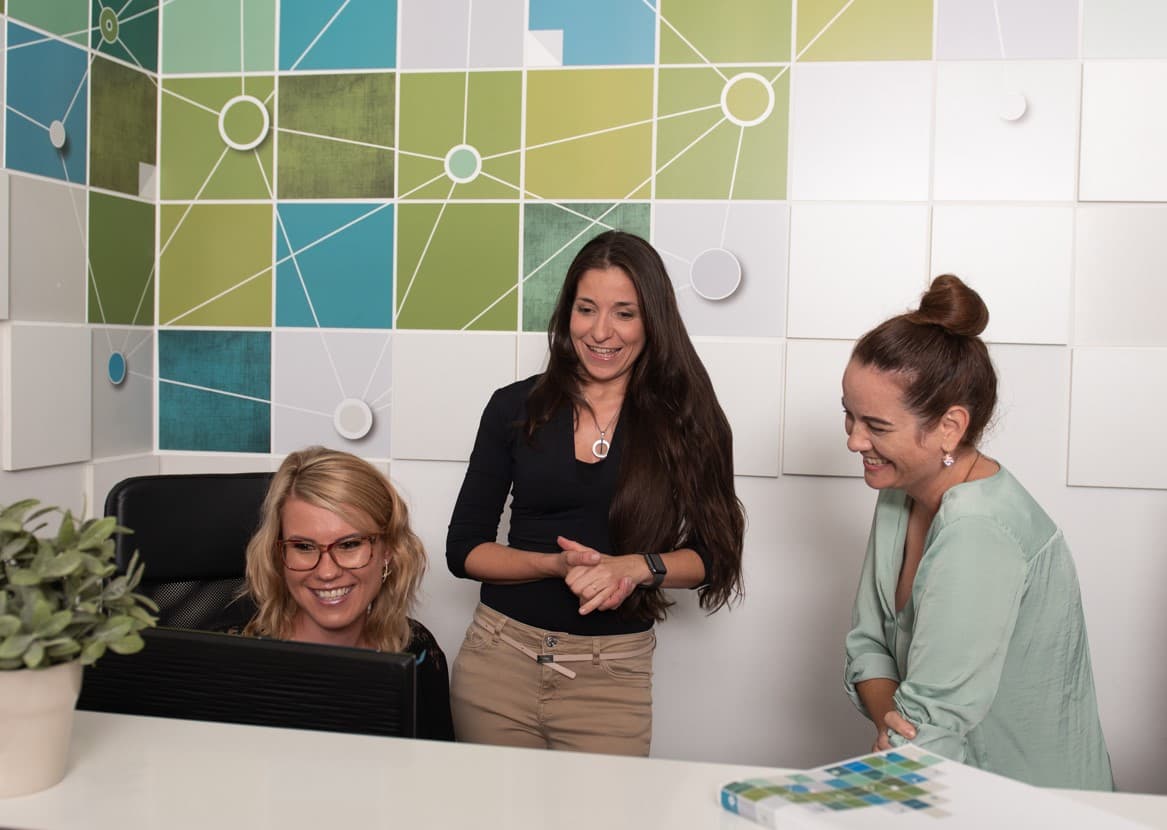 Three FX Software colleagues smiling while reviewing work at a desk